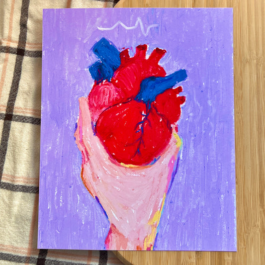 hand holding anatomical heart with purple background on a wooden and plaid surface