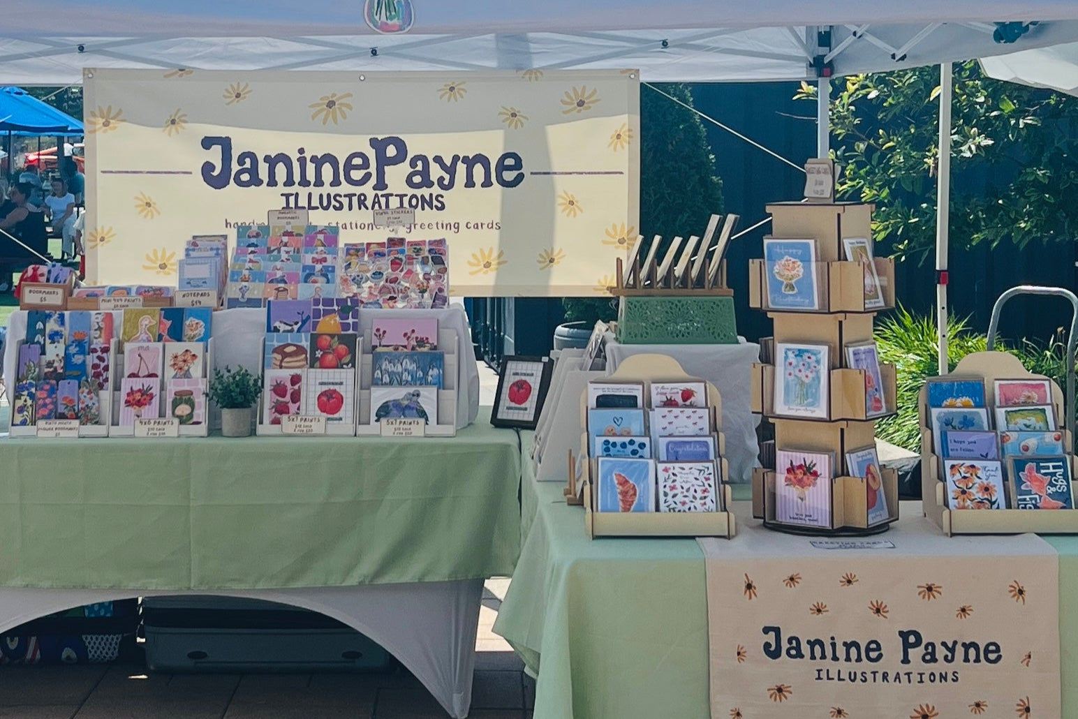 Janine Payne Illustrations booth with display of cards and stationery at an outdoor event.