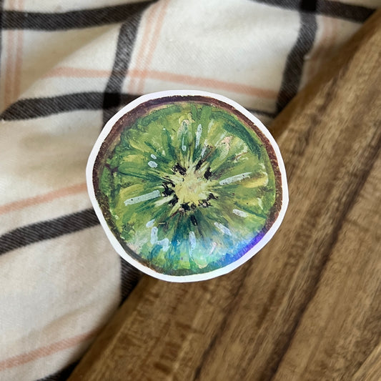 Sticker of a kiwi slice on a wooden surface with a plaid fabric background