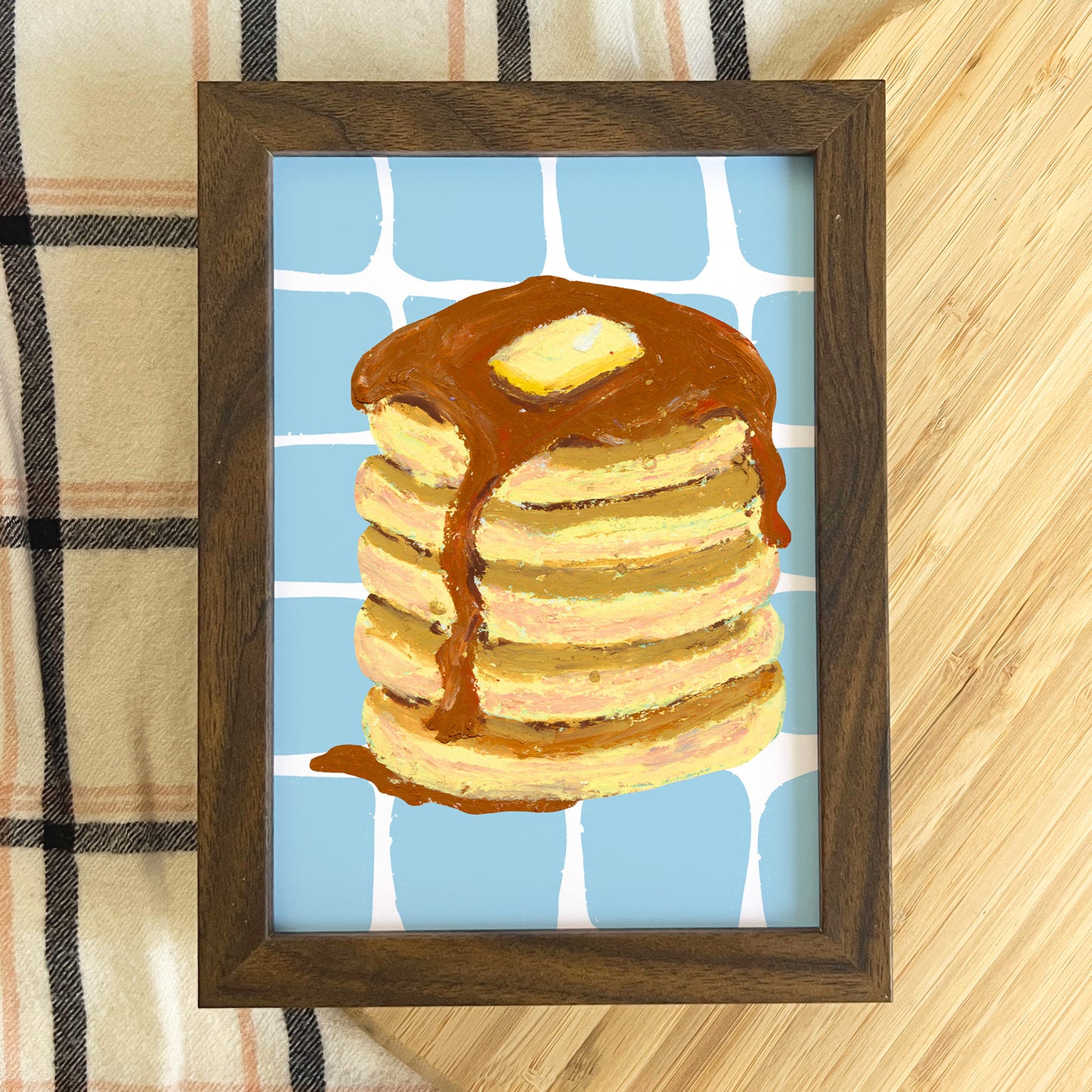 Framed artwork of a stack of pancakes with syrup on a checkered fabric background