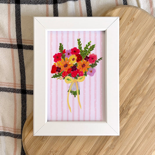 Framed artwork of a colorful bouquet on a wooden surface with plaid fabric in the background