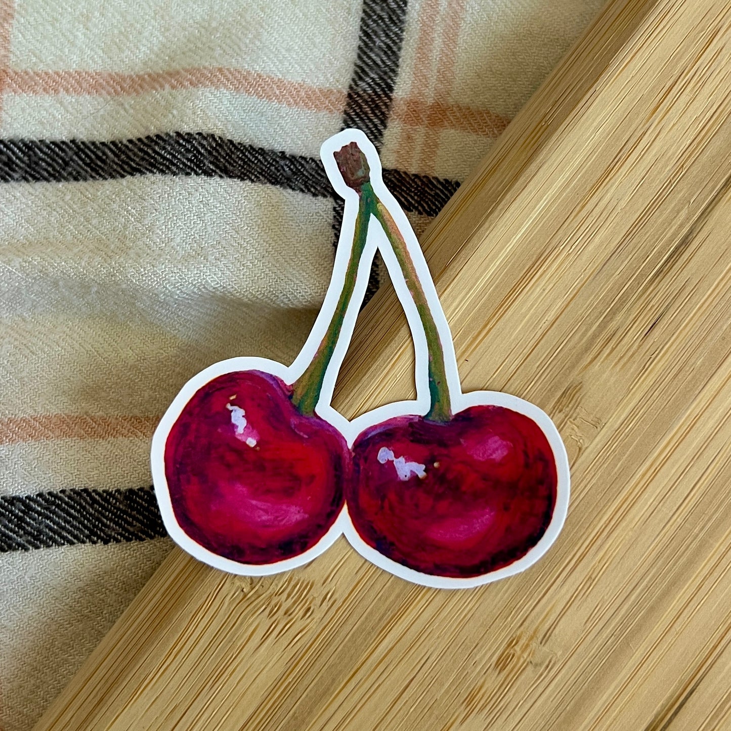 Sticker of two cherries on a wooden surface with plaid fabric background