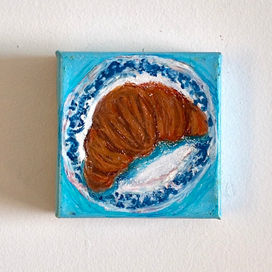 Painting of a croissant on a white and blue plate with blue background hanging on a wall