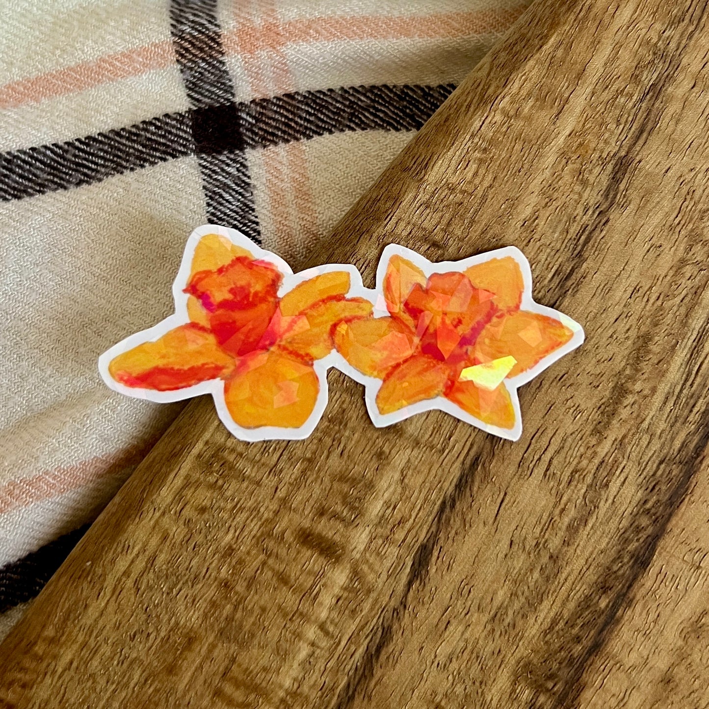 Two orange floral stickers on a wooden surface with a plaid fabric background