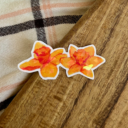 Two orange floral stickers on a wooden surface with a plaid fabric background