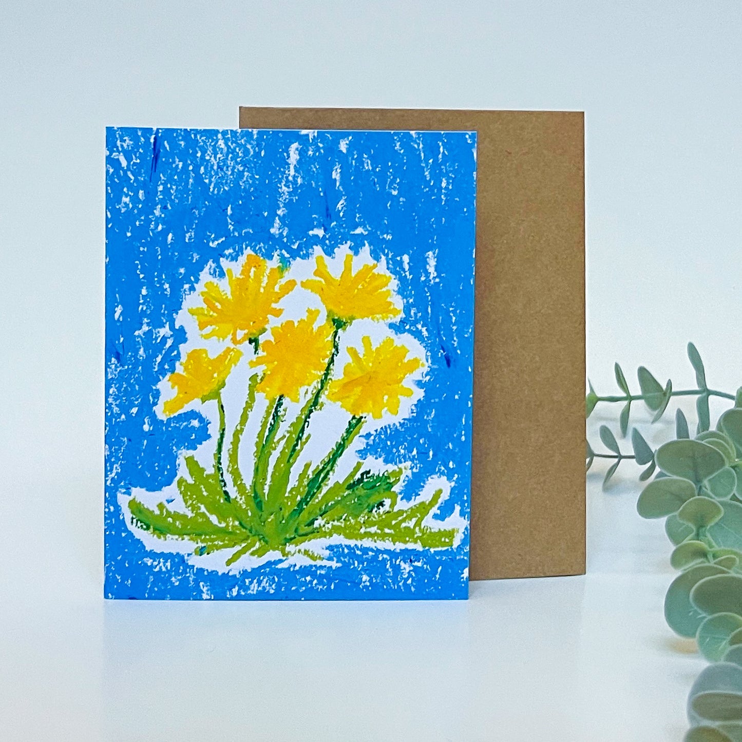 Greeting card with yellow flowers on a blue background, placed on a white surface with a light blue background.