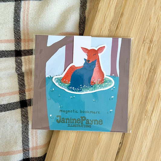 Magnetic bookmark with a deer and cat illustration by Janine Payne on a wooden surface.