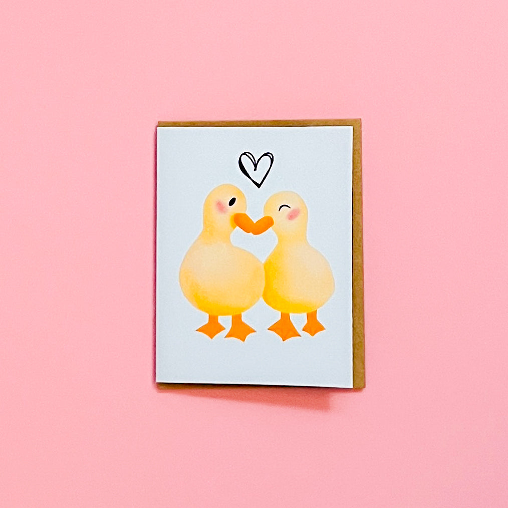 Card with two ducks hugging and a heart on a pink background