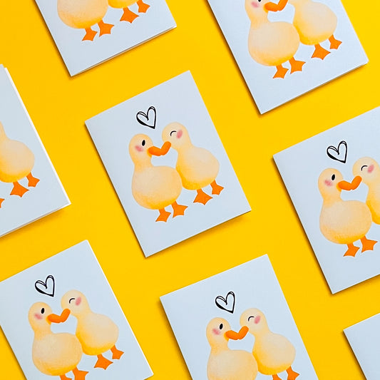 Illustrations of ducks on greeting cars with heart shapes on a yellow background