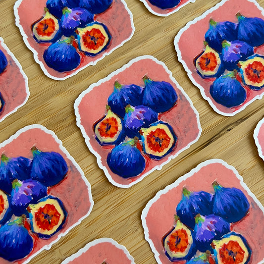 Stickers with blue and orange fig illustrations on a pink background, arranged on a wooden surface.