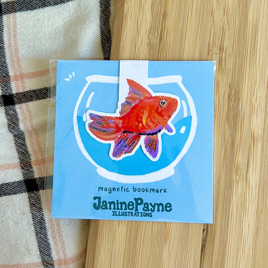 Magnetic bookmark with a fish illustration by Janine Payne on a wooden surface.
