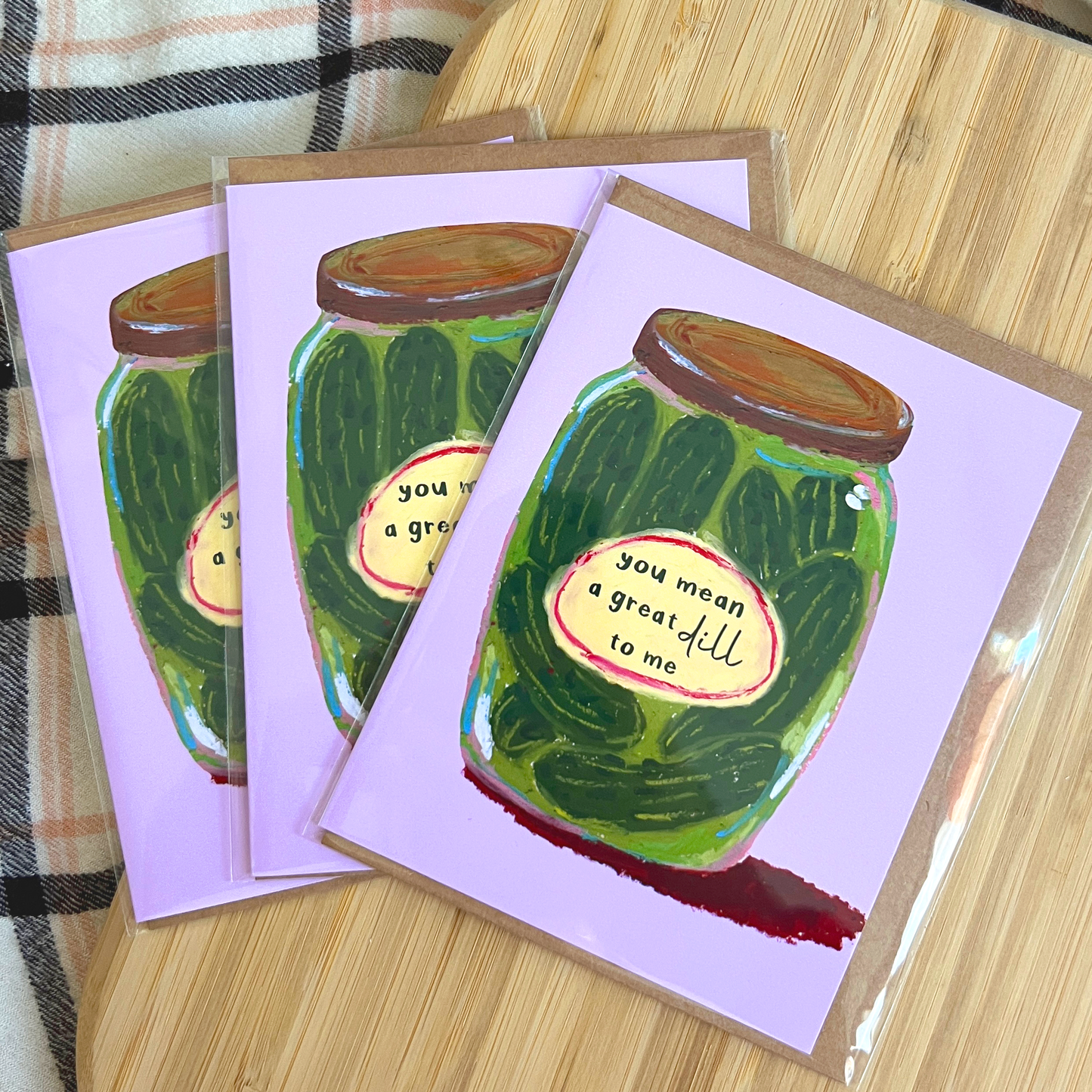 Three greeting cards with pickle jar illustrations on a wooden surface.