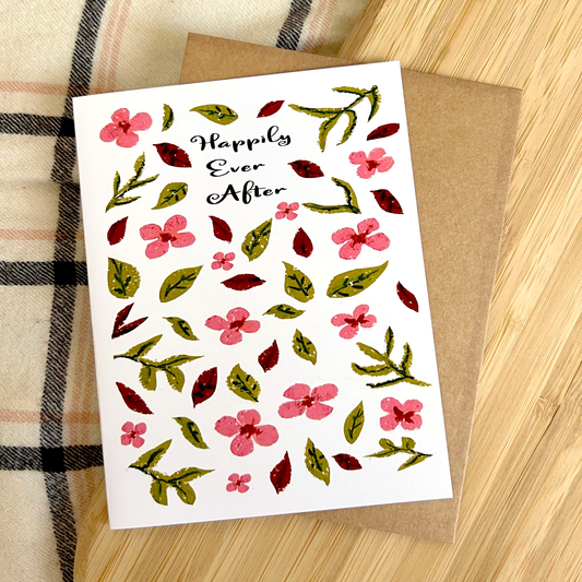 Greeting card with floral design and 'Happily Ever After' text on a wooden surface.