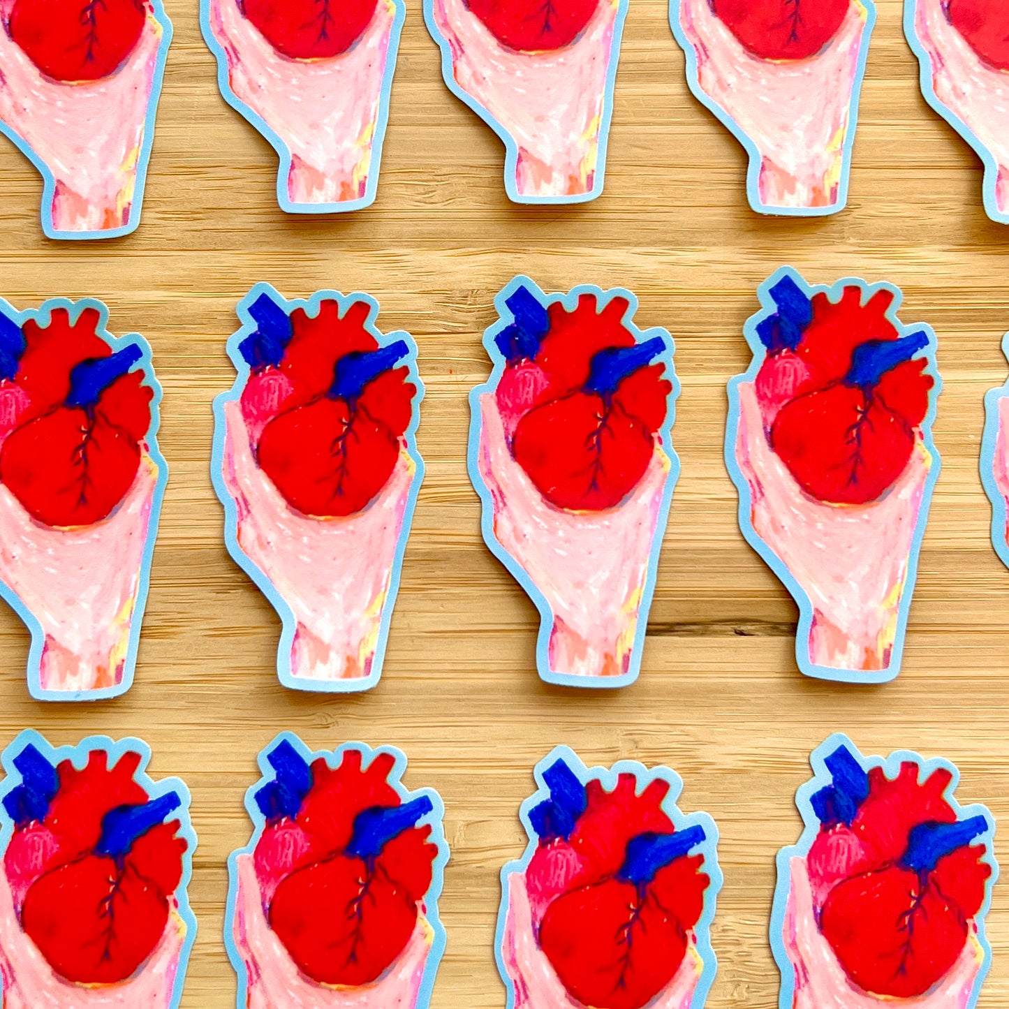 Stickers of hands holding anatomical hearts on a wooden surface