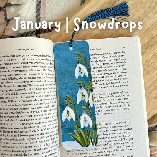 Book with a snowdrop-themed bookmark on a wooden surface, with 'January Snowdrops' text overlay.