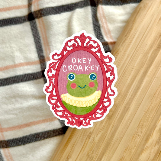 Sticker with a frog in a decorative frame on a plaid fabric background