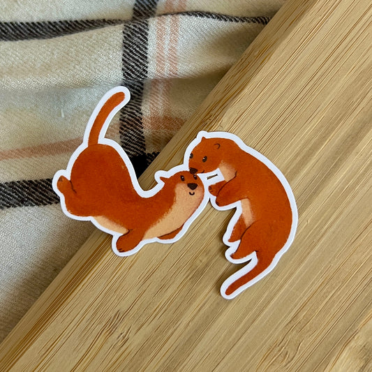 Two cartoon otters on a wooden surface with plaid fabric in the background