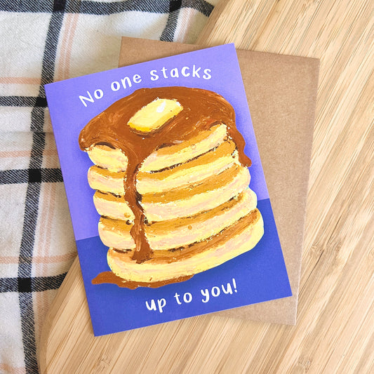Card with a stack of pancakes and text 'No one stacks up to you!' on a wooden surface