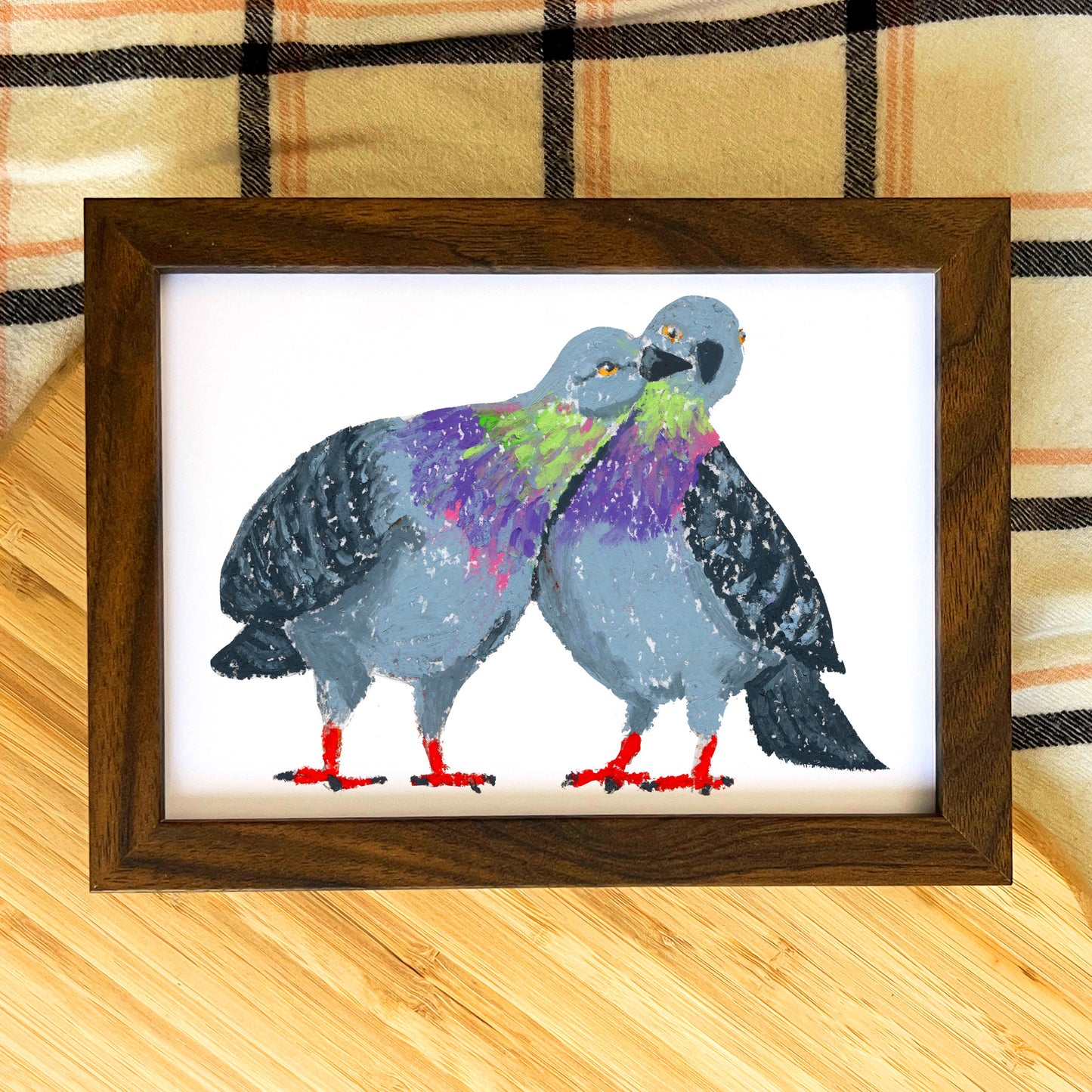 Framed artwork of two stylized pigeons on a wooden surface with plaid fabric background