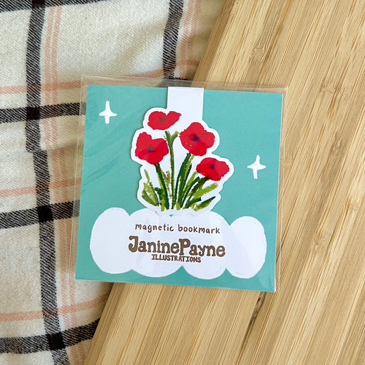 Magnetic bookmark with red flowers and 'Janine Payne Illustrations' text on a wooden surface.