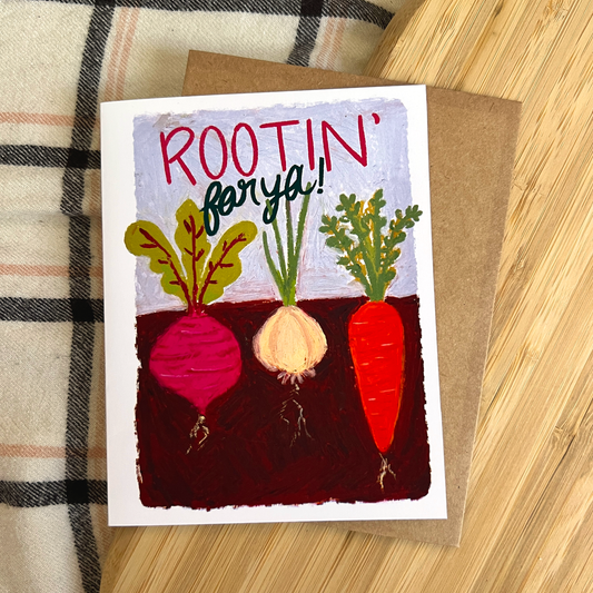 Greeting card with root vegetables illustration and text 'ROOTIN' FOR YA!' on a wooden surface.