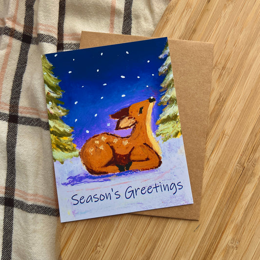 Greeting card with a deer illustration and 'Season's Greetings' text on a wooden surface.