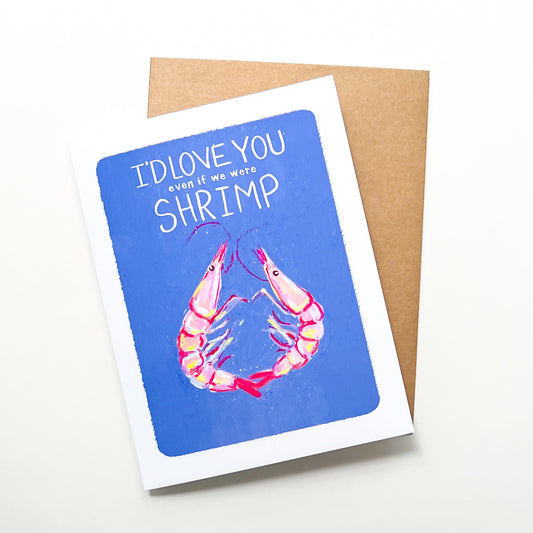 Greeting card with shrimp illustration and text 'I'd love you even if we were shrimp' on a blue background, with a brown envelope.