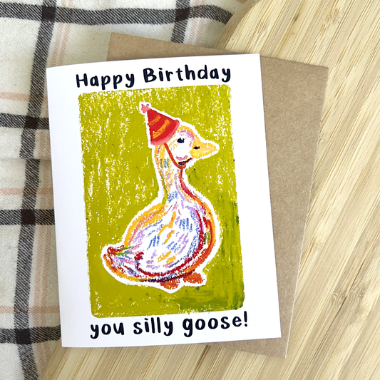 Birthday card with a goose wearing a party hat on a wooden surface