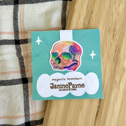 Magnetic bookmark with colorful skull design and 'Janine Payne Illustrations' text on a wooden surface.