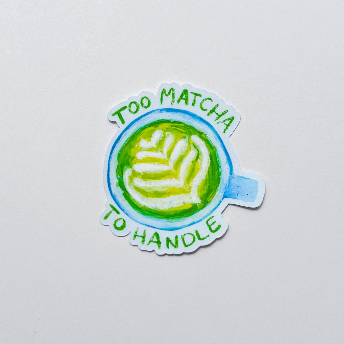 Sticker with a matcha latte design and text 'Too Matcha To Handle' on a light gray background