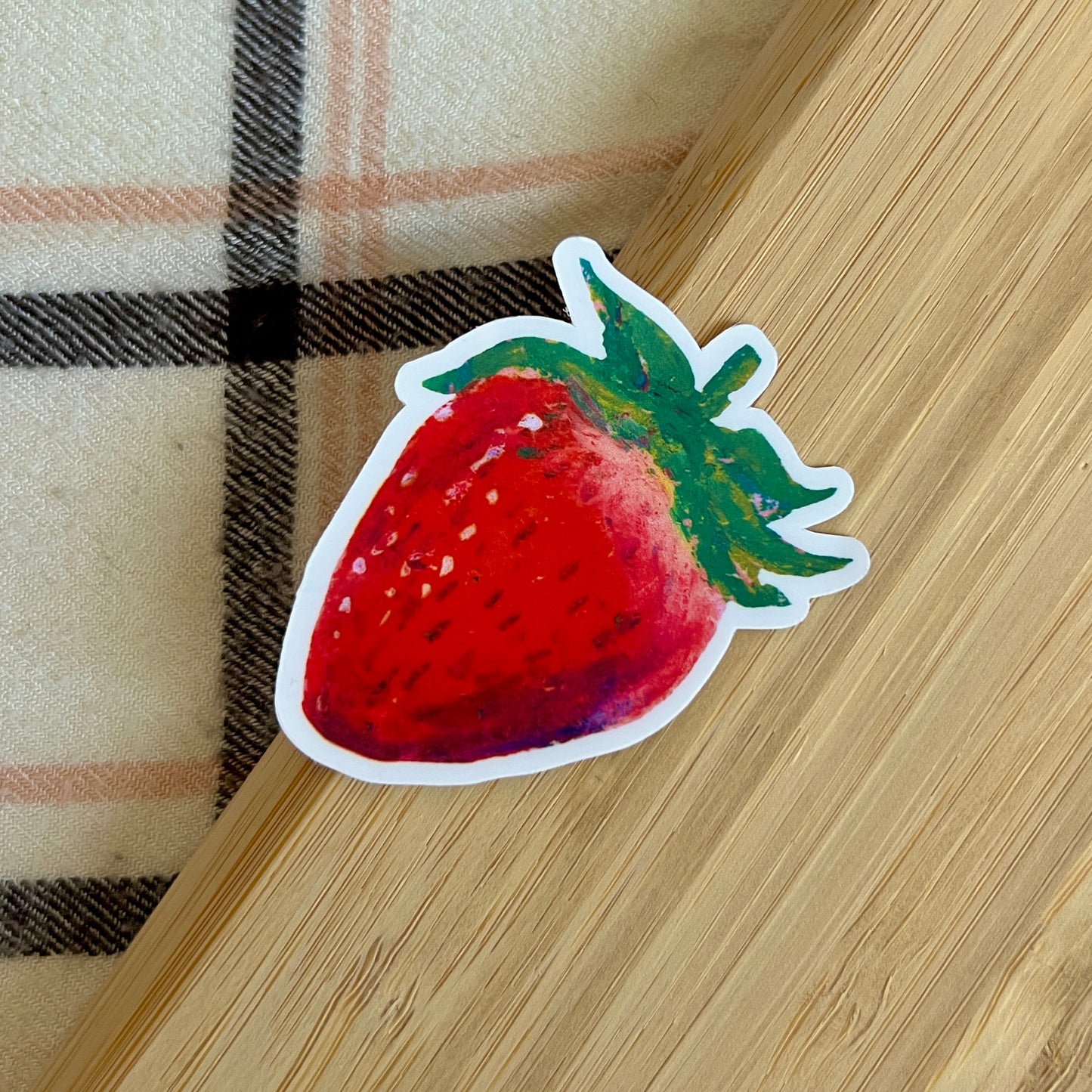 Strawberry-shaped sticker on a wooden surface with plaid fabric background