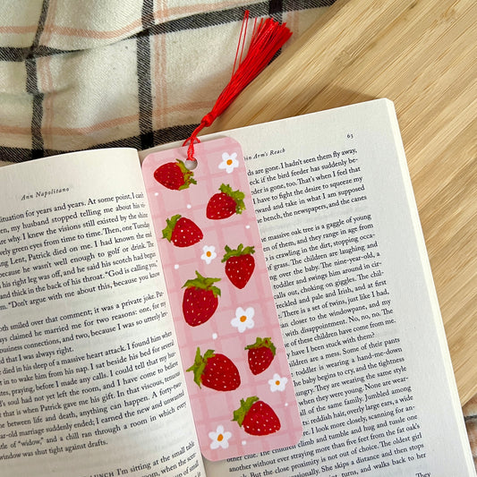 Pink strawberry-themed bookmark on an open book with a red string