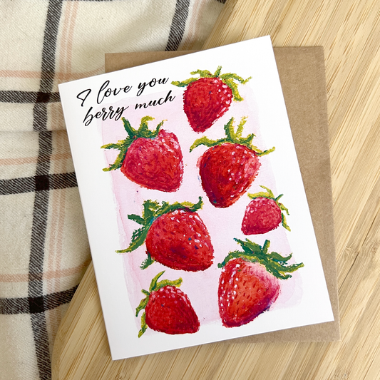 Greeting card with strawberries and 'I love you berry much' text on a wooden surface.
