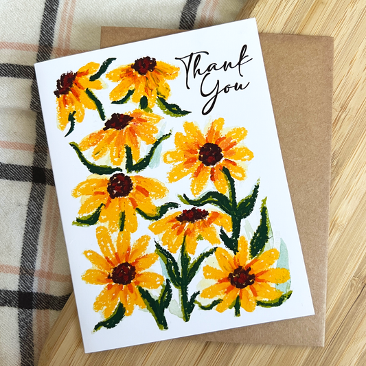 Greeting card with yellow flowers and 'Thank You' text on a wooden surface.