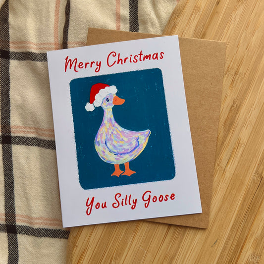 Christmas card with a goose wearing a Santa hat on a wooden surface.