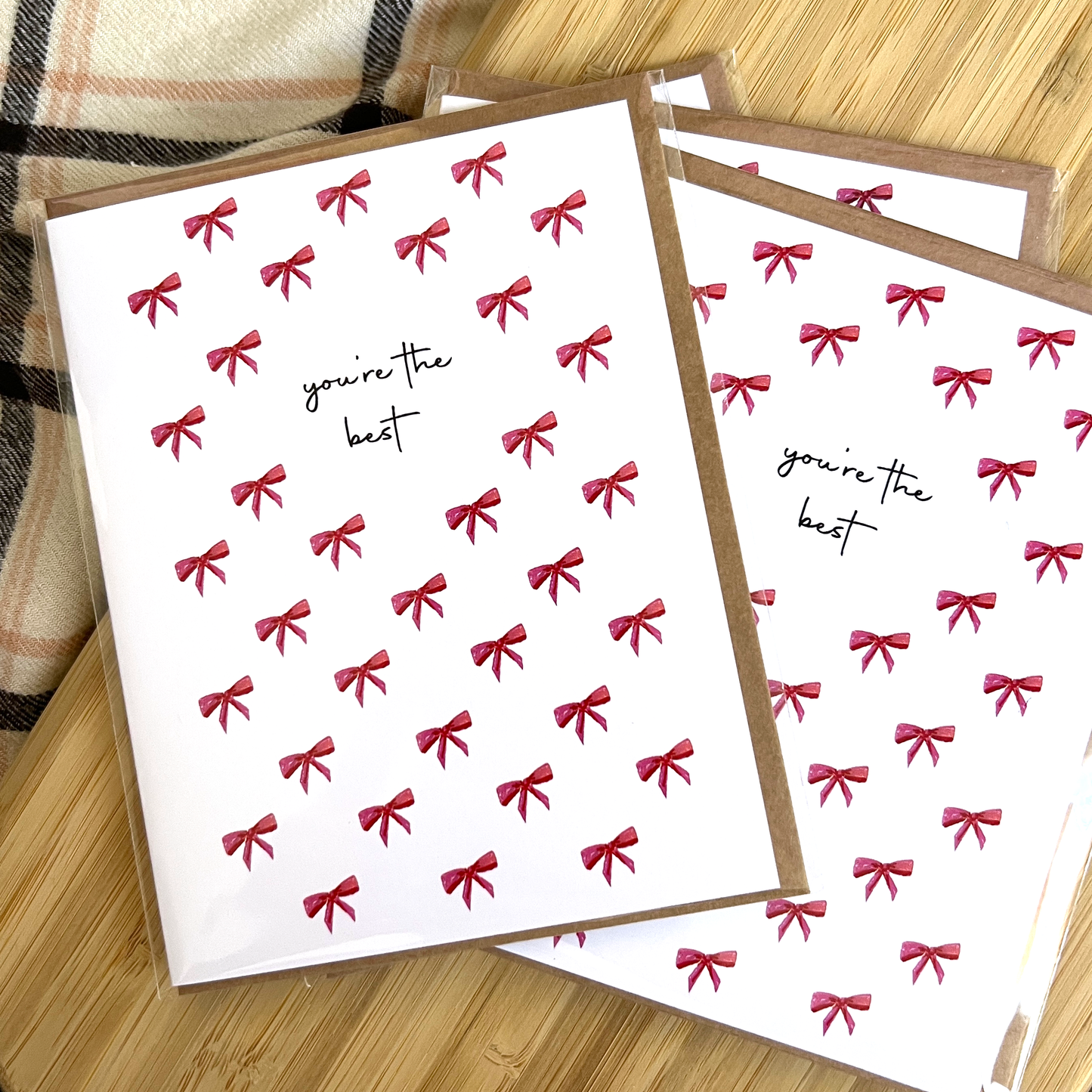 Greeting cards with red bows and 'you're the best' text on a wooden surface.
