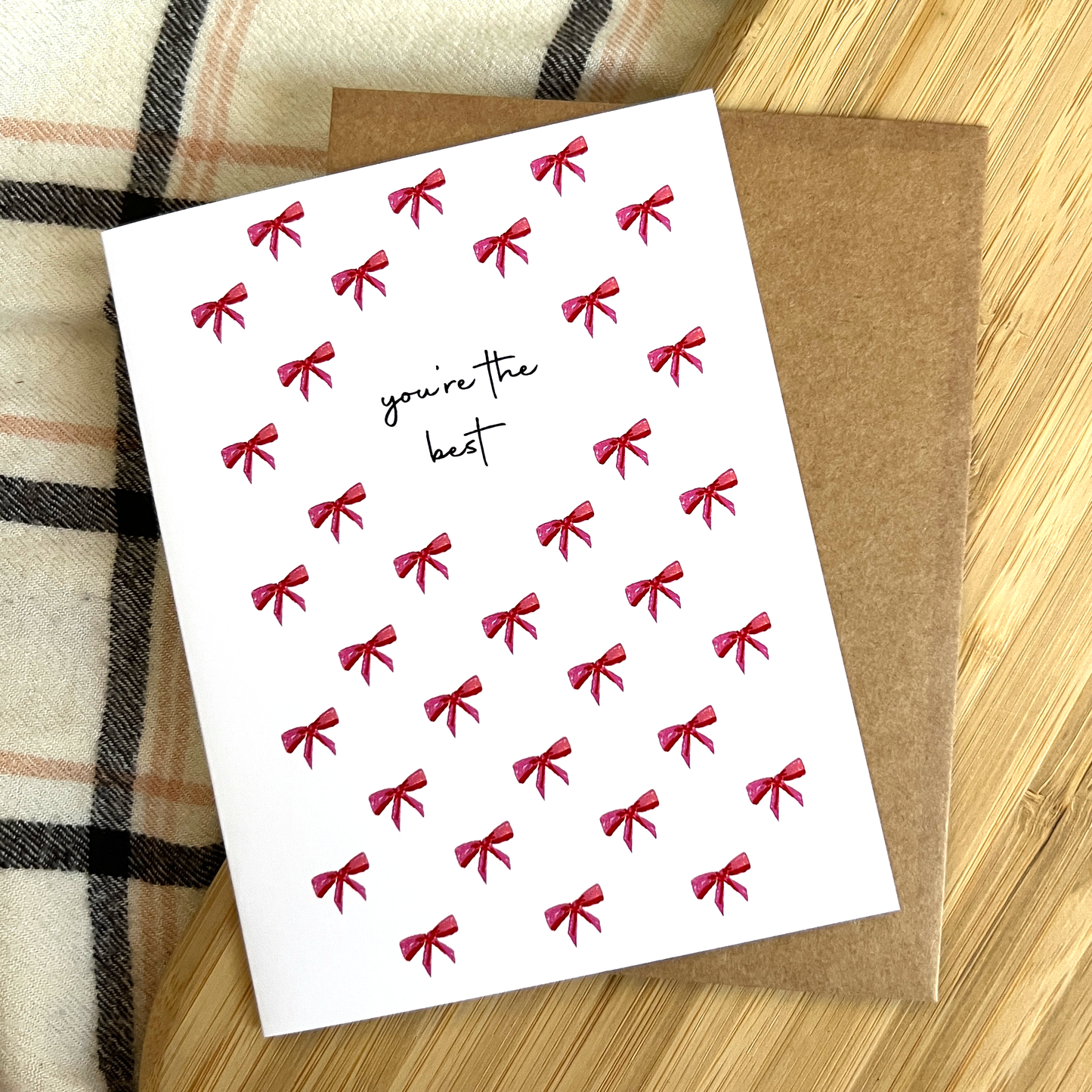 Greeting card with red bows and 'you're the best' text on a wooden surface