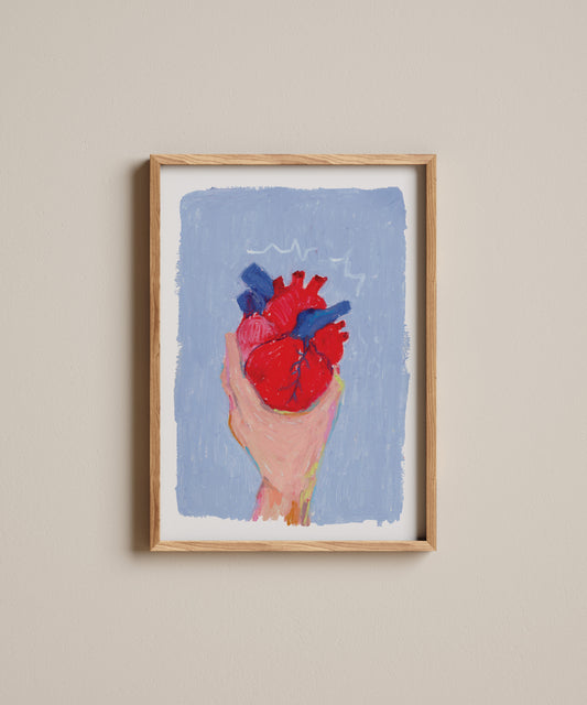 Framed artwork of a hand holding a red heart against a blue background on a beige wall.