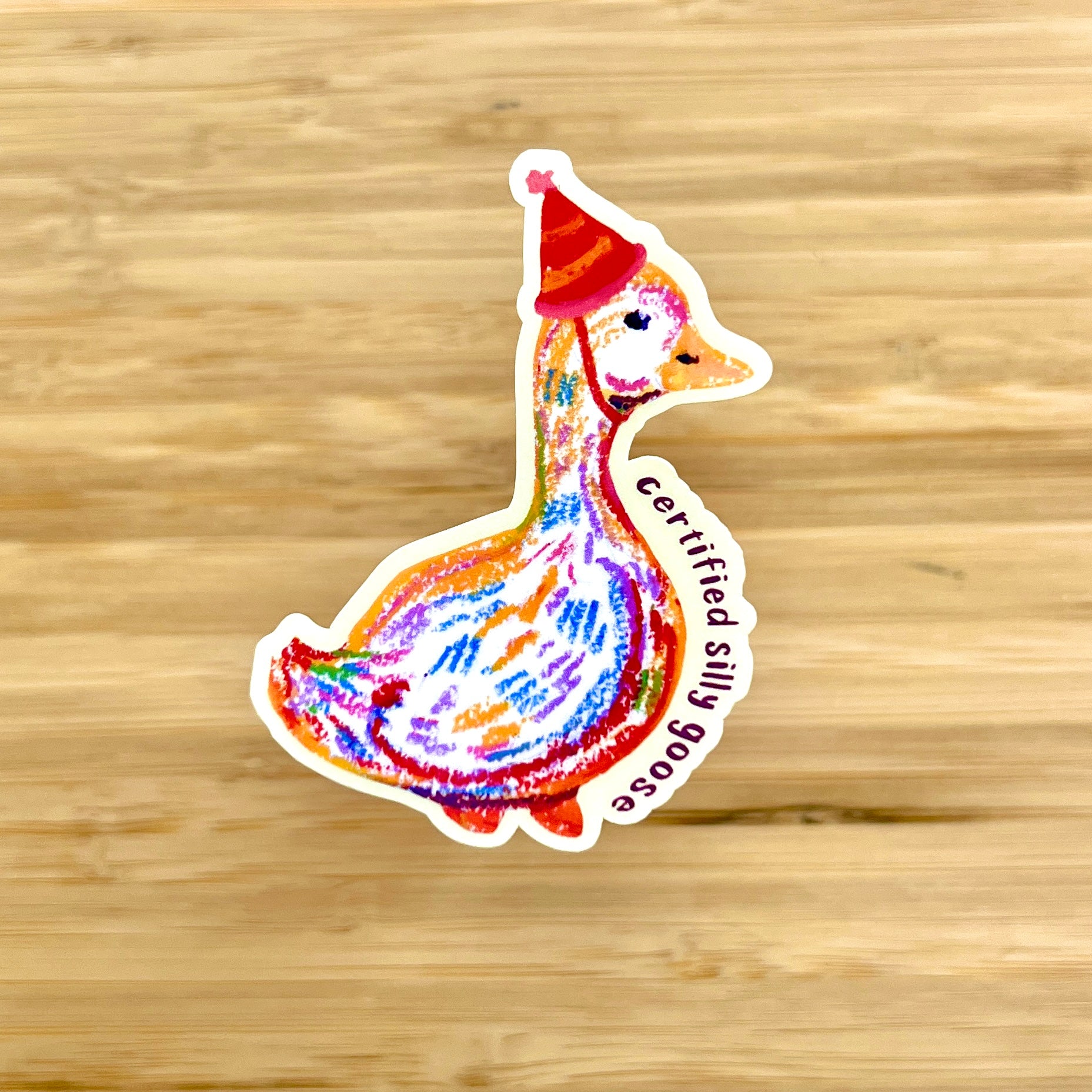 Colorful sticker of a goose wearing a red hat on a wooden surface