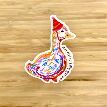 Colorful sticker of a goose wearing a red hat on a wooden surface