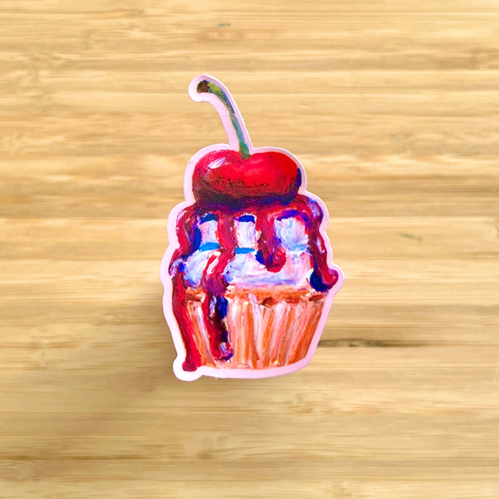 Sticker of a cupcake with a cherry on top on a wooden surface