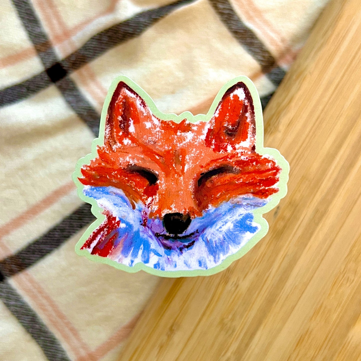 Sticker of a fox face with red and blue colors on a checkered fabric background