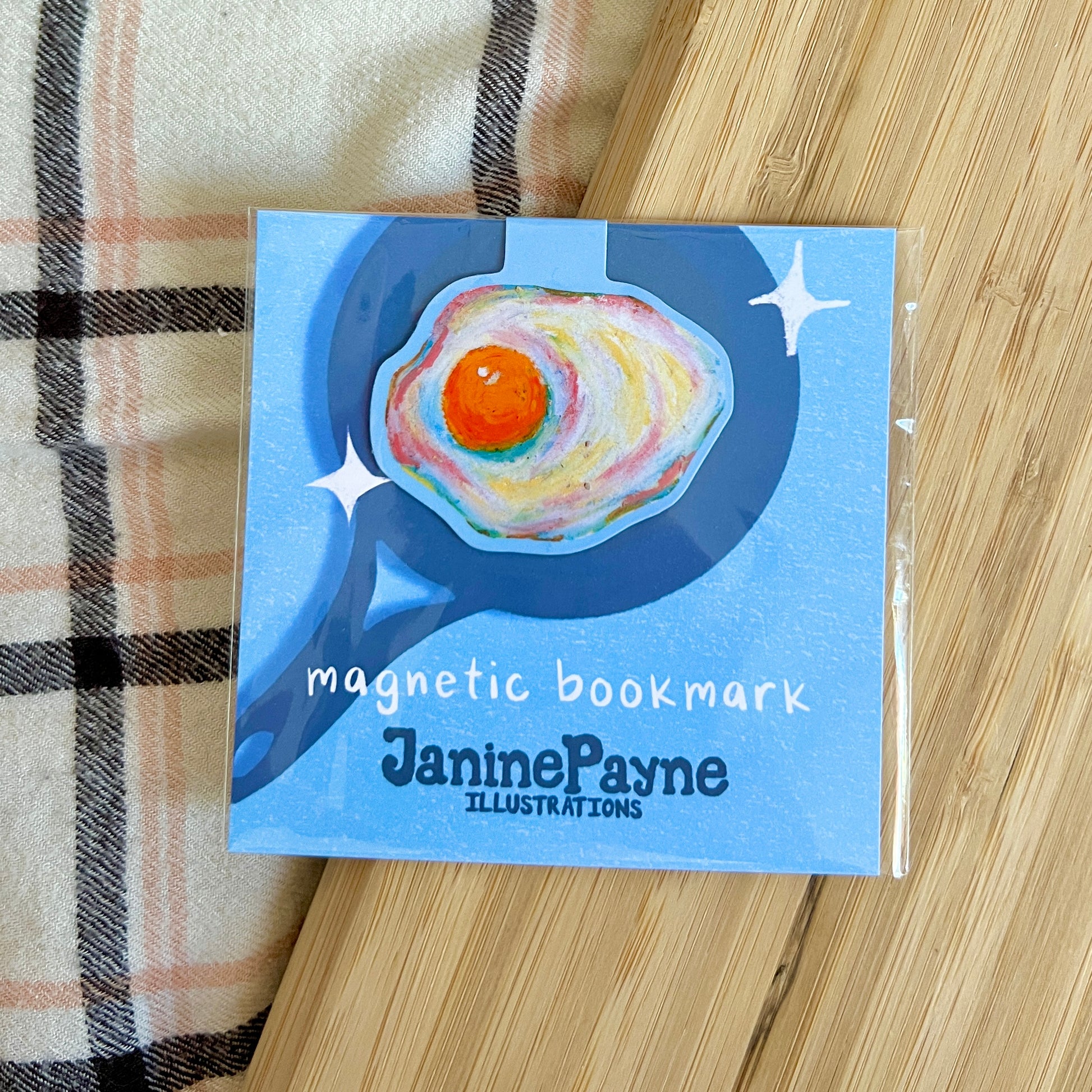 Egg magnetic bookmark with Janine Payne illustrations on a wooden surface