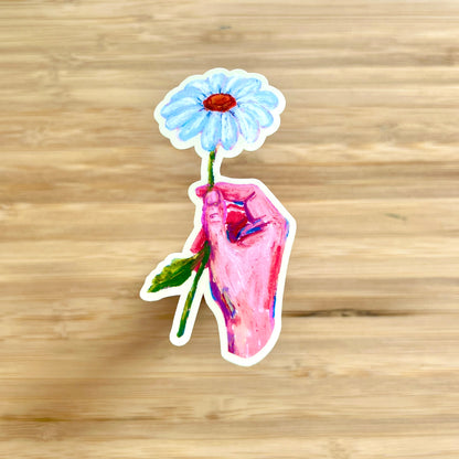 hand holding daisy sticker on wooden surface