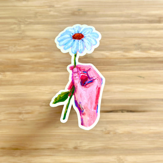 hand holding daisy sticker on wooden surface