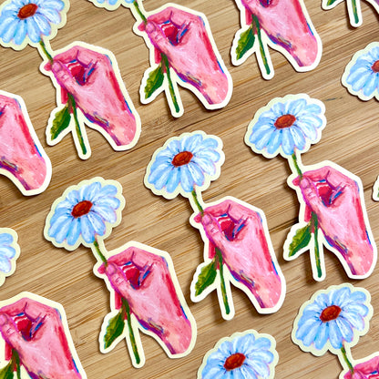 Stickers of hands holding white daisies on a wooden surface