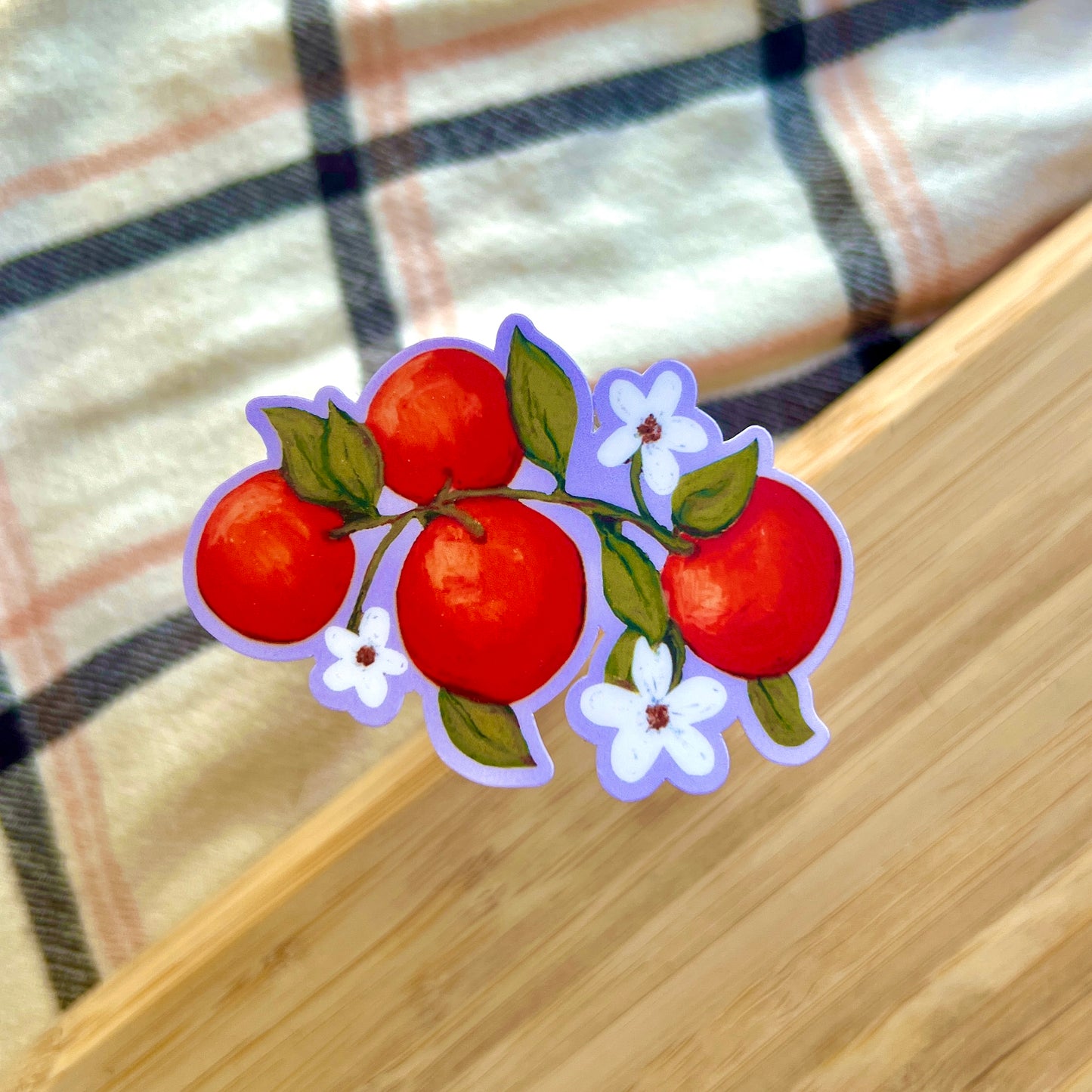 Sticker of oranges and white flowers on a wooden surface with plaid fabric background
