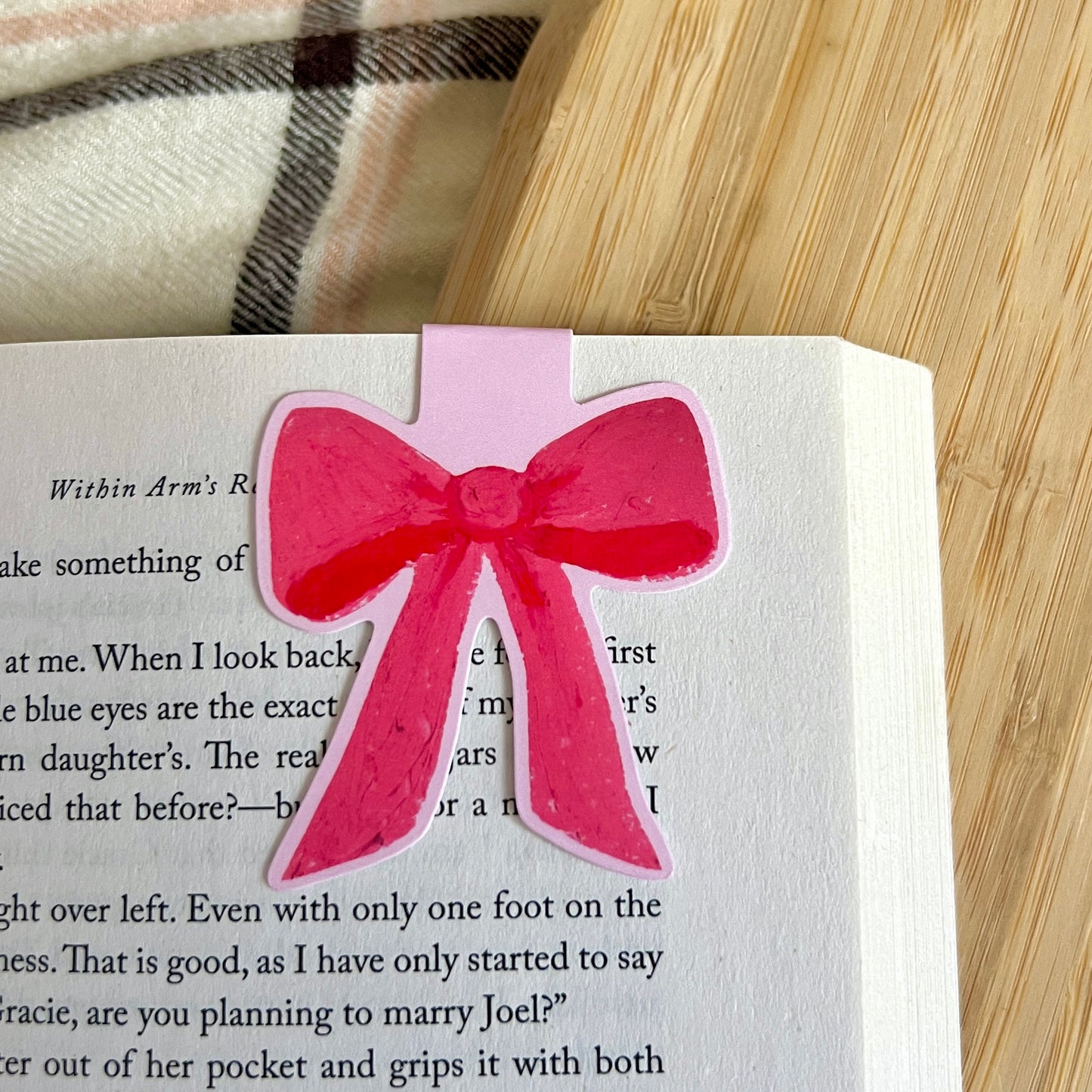 Pink bow bookmark on a book with a plaid fabric background