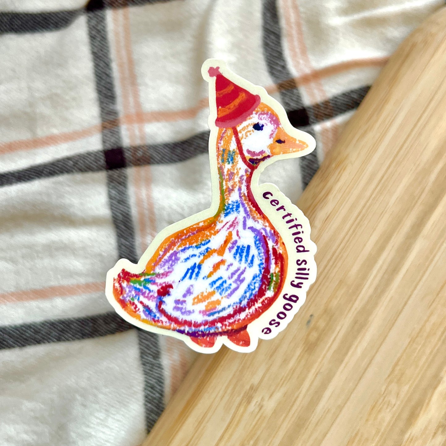 Colorful sticker of a goose wearing a red hat with 'Certified Silly Goose' text on a plaid fabric background.
