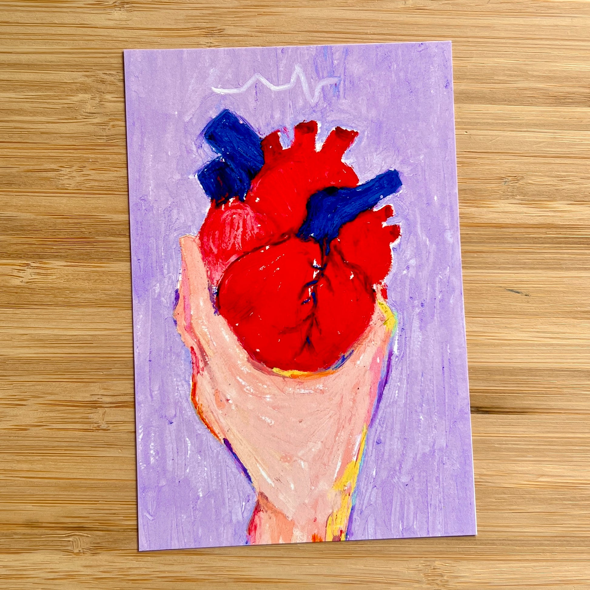 hand holding anatomical heart with purple background on wooden surface